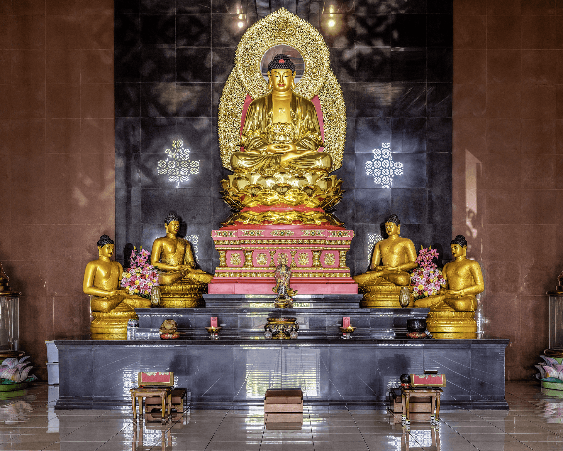 Patung Buddha emas di Vihara Griya Vipassana Avalokitesvara, dikelilingi oleh patung-patung kecil dan persembahan bunga.